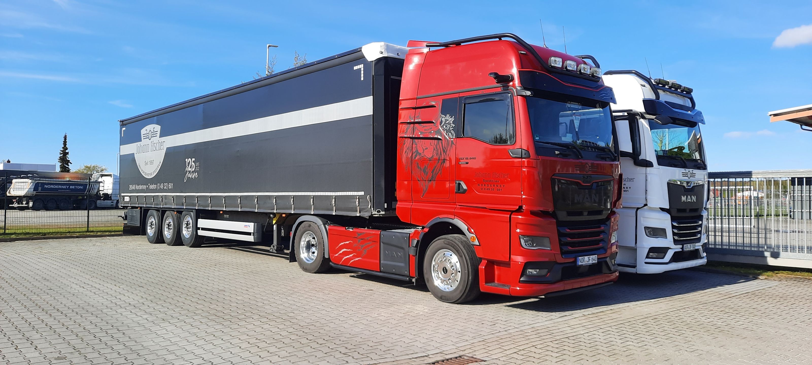 Auf dem Bild sind zwei LKW der Johann Fischer KG zu sehen, einer ist rot und der anderen weiß